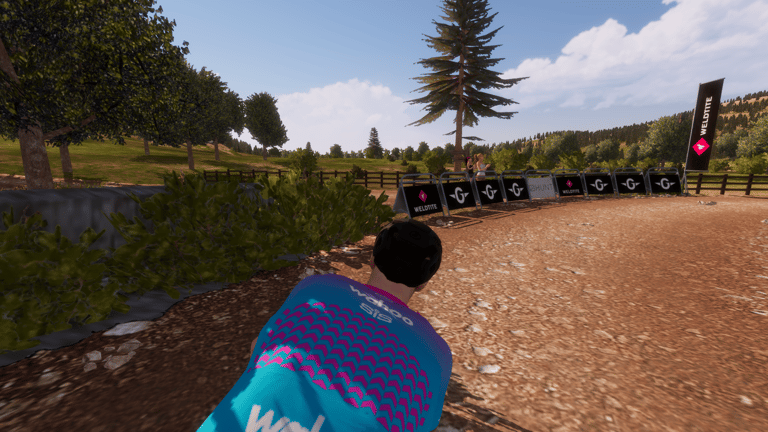 Virtual rider on a gravel road in the RGT Cycling app, beside Weldtite and Genesis barriers on the Dirty Reiver course.