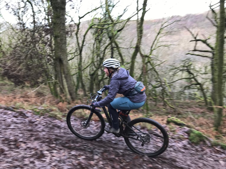 Rider in a Findra Stroma jacket and helmet on a mountain bike along a muddy woodland track in the Quantocks.