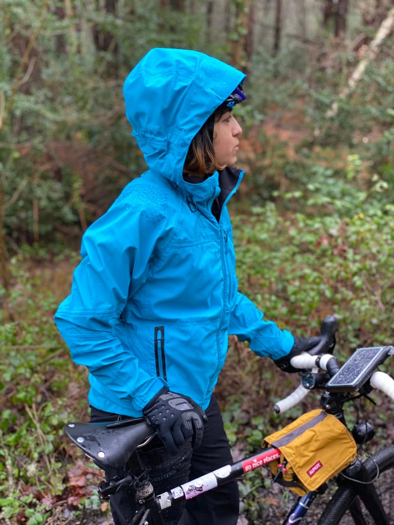 Side view of the Madison DTE jacket's helmet-compatible hood pulled up over a cycling helmet beside a gravel bike.