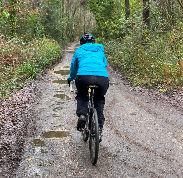 Vedangi Kulkarni rides away up a puddled woodland track in the blue Madison DTE waterproof jacket.