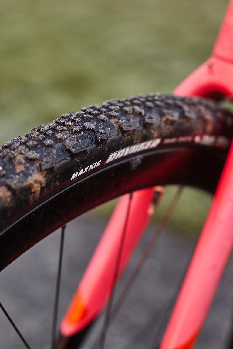 Maxxis Ravager 700 x 40 gravel tyre with mud packed between the knobs, sitting between the pink fork legs.