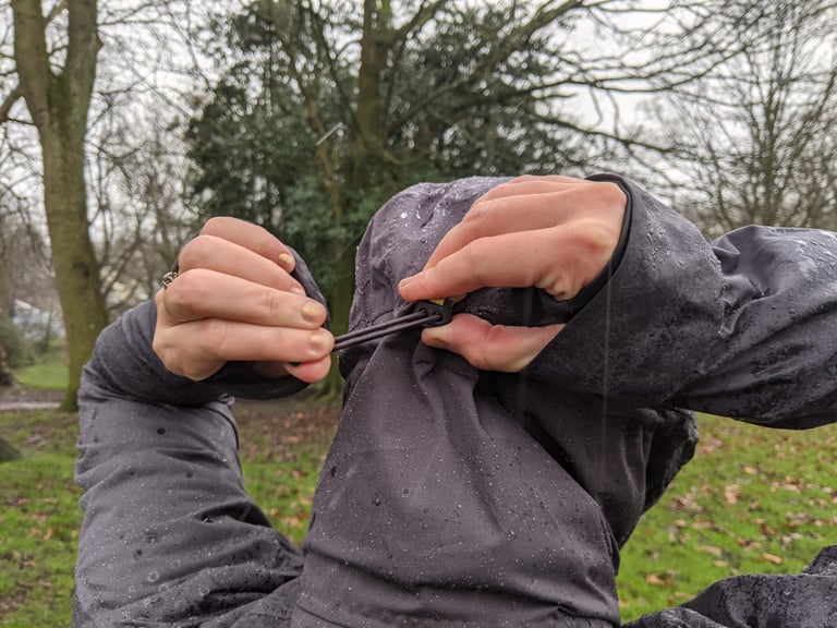 Findra Stroma hood adjusted with a single drawcord at the back, hands pulling the cord tight in the rain.