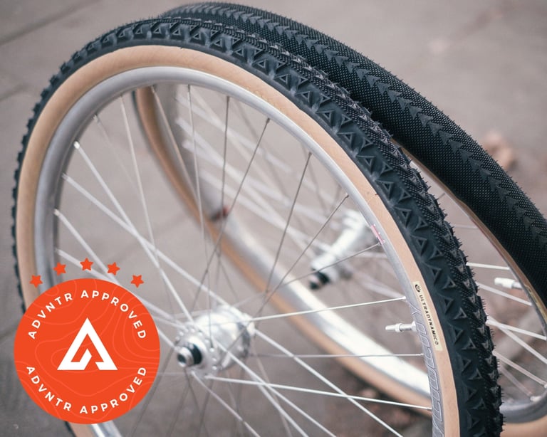 Ultradynamico Rosé and Cava tyres with tan sidewalls on two silver-rimmed wheels stood on a pavement.