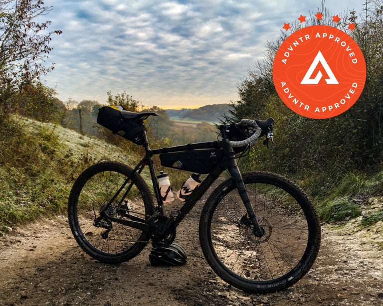 Bombtrack Hook EXT-C gravel bike with frame, saddle and bar bags on a frosty track above open countryside.