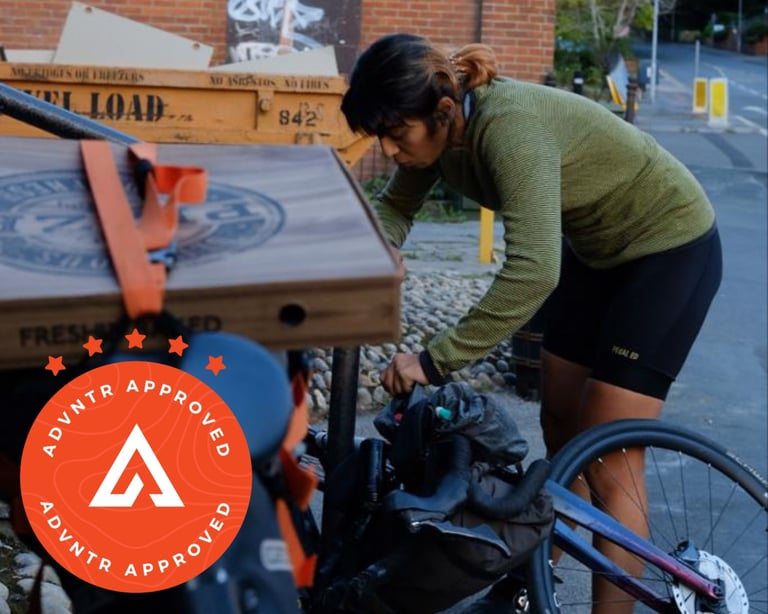 Rider in a green striped Findra merino base layer packs bags on a loaded bike beside a skip on a street.