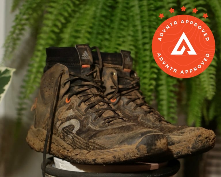 Muddy Five Ten Trailcross Mid Pro flat-pedal shoes on a stool in front of a fern.