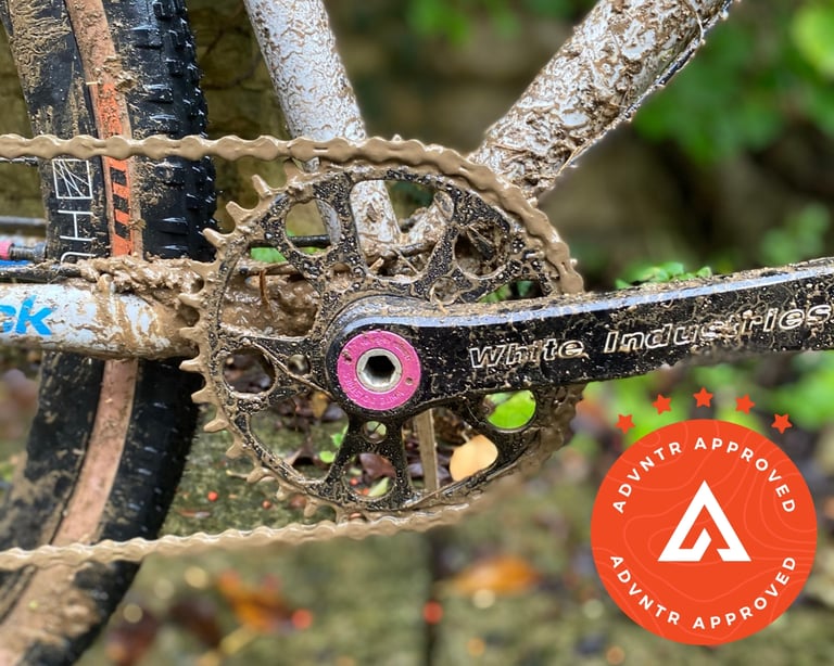 White Industries G30 crank and chainring with a pink extractor bolt on a mud-caked gravel bike.