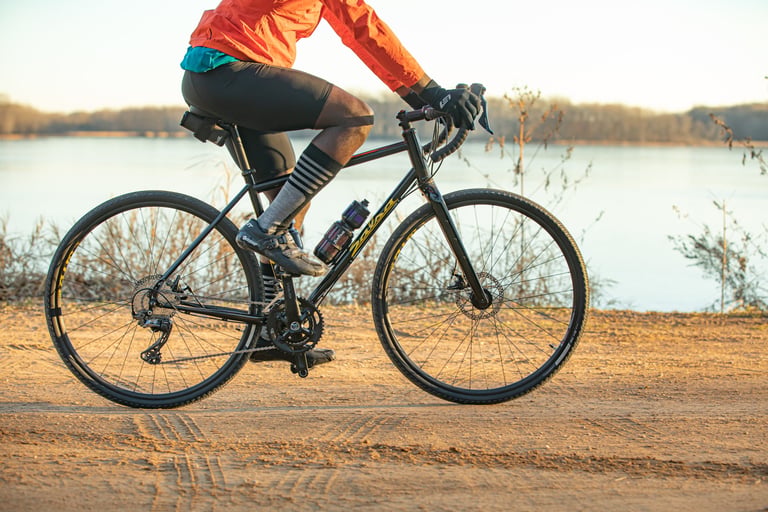 Rider on the 2021 Salsa Vaya GRX 600 on a sandy dirt road beside a lake, with a bottle in the frame.