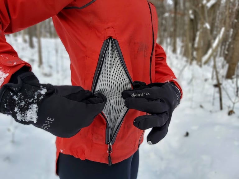 Side vent of the Showers Pass Refuge jacket unzipped to show the mesh panel, held open by gloved hands.