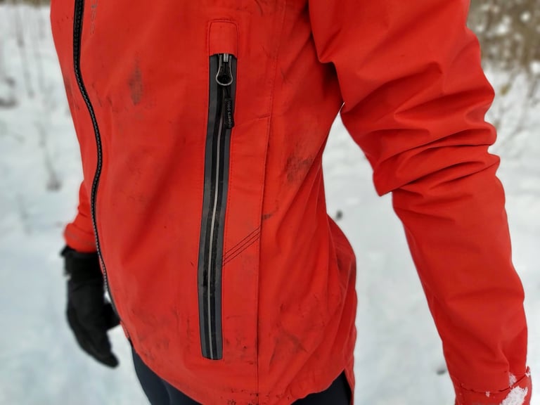 Close-up of the long side zip on the red Showers Pass Refuge jacket, where the pocket and vent zips sit together.