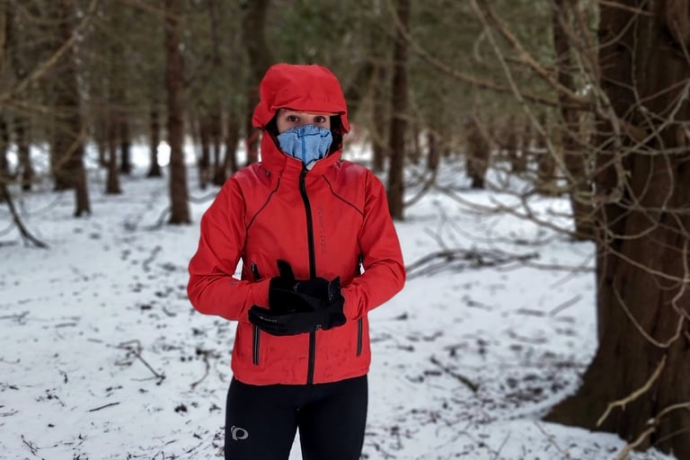 Rider wearing the Showers Pass Refuge jacket with its hood up and a face covering in snowy woodland.