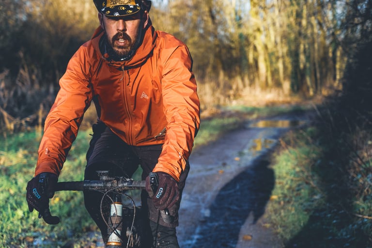 Rider in the 7mesh Copilot jacket and a patterned cap on a bike along a muddy winter track with puddles.