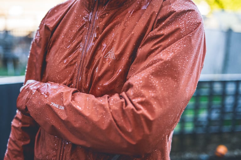 Water beading on the DWR-treated fabric of the 7mesh Copilot jacket, arms folded to show the sleeve print and chest logo.