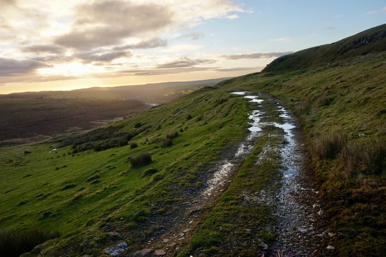 Puddled stony track along a grassy ridge at sunrise above Merthyr on day one of the Festive 500.