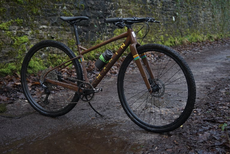 Small-frame Marin DSX 2 with 700c wheels on a muddy track beside a mossy wall, showing its slanted top tube.