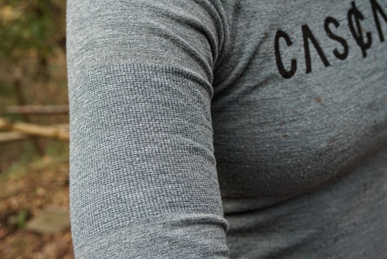 Close-up of the textured sleeve panel on a grey Cascada merino baselayer, with the logo at the chest.