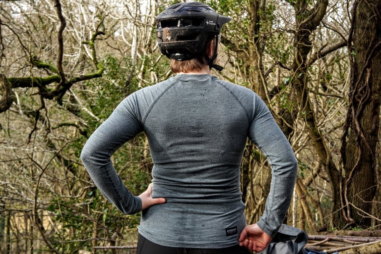 Back view of a rider in a grey long sleeve Cascada merino baselayer, showing how far it reaches down the torso.