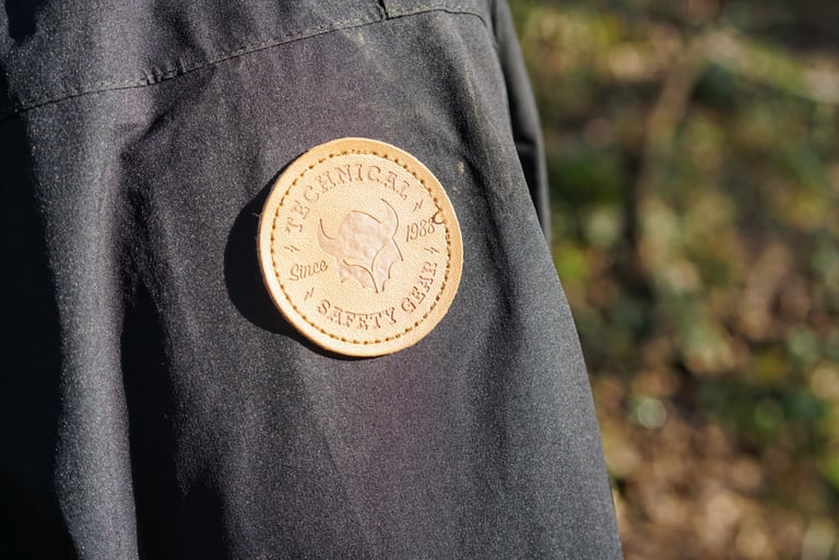 Faux leather Technical Safety Gear patch on the upper left sleeve of the black TSG Drop Rain Jacket.