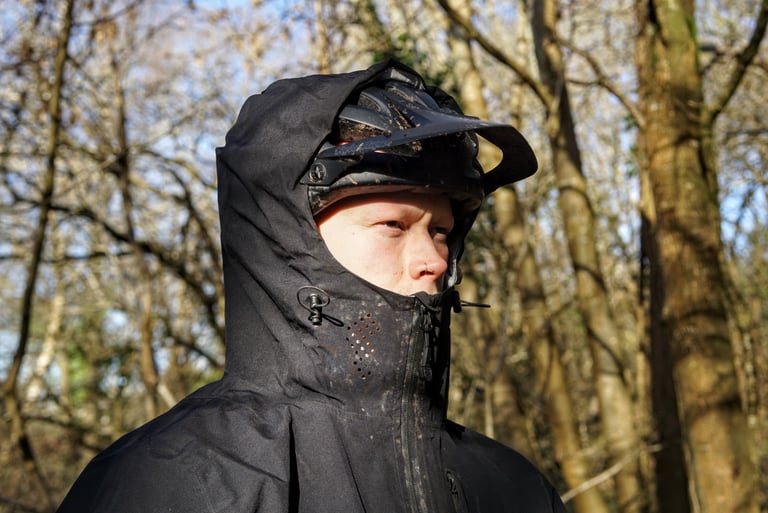 TSG Drop Rain Jacket hood worn over a peaked mountain bike helmet, with perforated collar vent and drawcord.