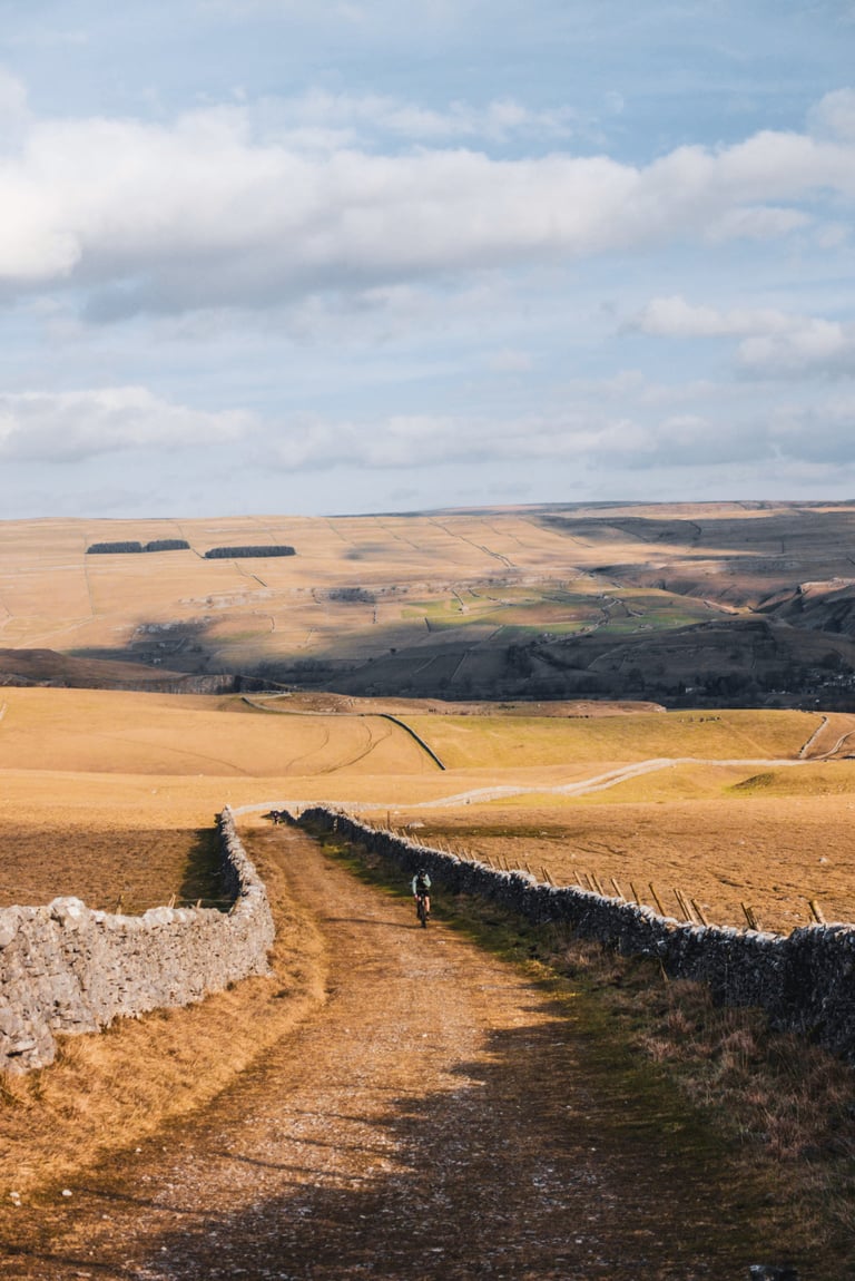 Rider on a stony track between dry-stone walls across open hills, from Restrap's UK gravel route catalogue.