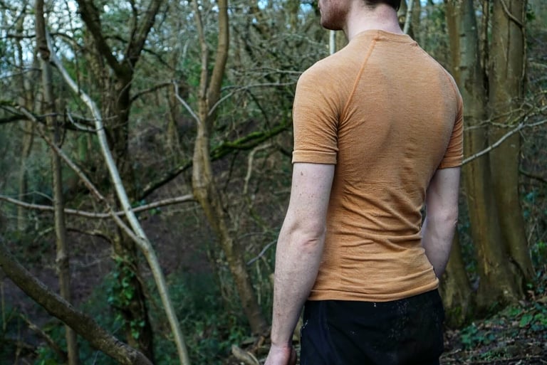 Back view of a rider in a peach short sleeve Cascada merino baselayer standing in woodland.