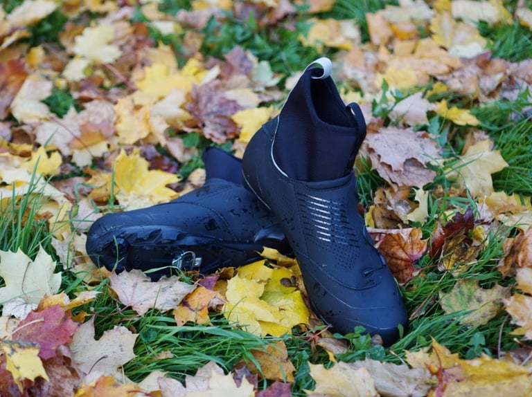 Black Northwave Magma XC Core shoe in the grass with reflective trim, and the second shoe on its side showing the cleat.