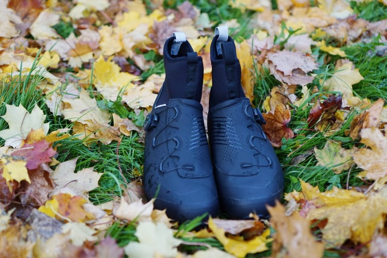 Front view of black Northwave Magma XC Core winter shoes with dial closures and pull loops, standing on fallen leaves.