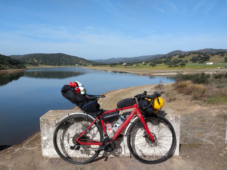 Norco Search with 32 mm slick tyres and bikepacking bags rests on a concrete block beside a reservoir in Spain.