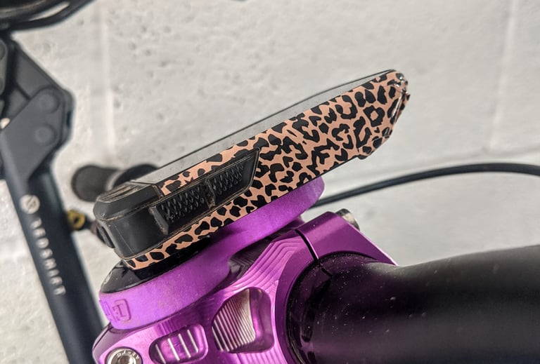 Wahoo ELEMNT ROAM in a leopard-print wrap kit, mounted on a purple stem-cap mount, side view.