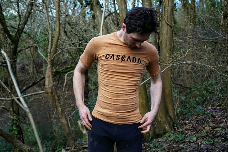 James in a peach short sleeve Cascada merino baselayer, looking down in woodland to check the fit.