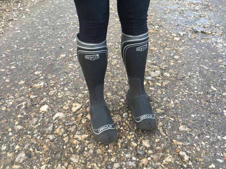 Front view of a rider standing in knee-high SPATZ GravlR overshoes with grey branded tops on a stony track.