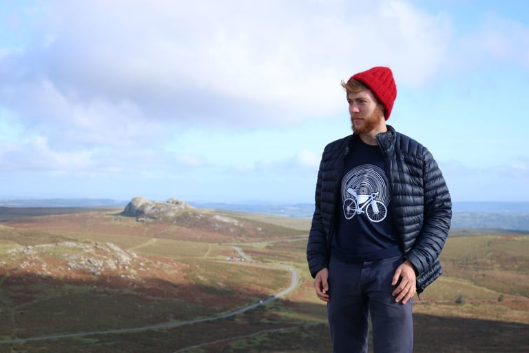 Ceri in a red beanie wears a Threads of Adventure bikepacking t-shirt on open moorland in the UK.