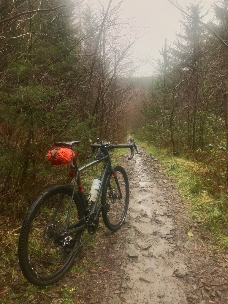 Gravel bike with an orange seat pack on a wet, rocky forest track in Llanwonno Forest.