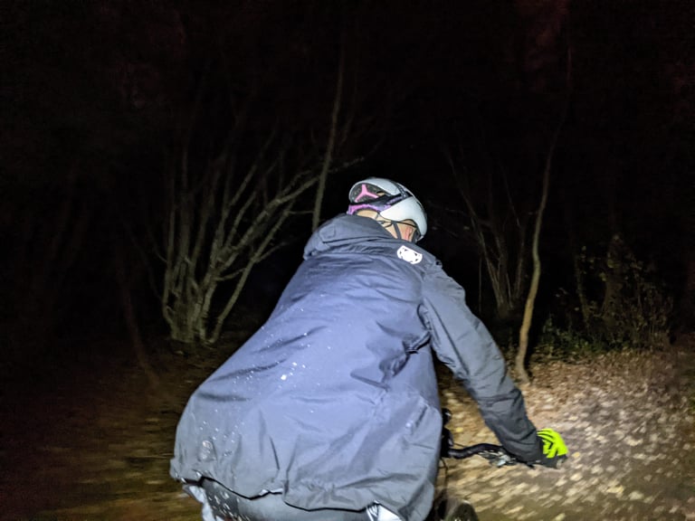 Rider on a night ride in the TSG Drop Rain Jacket, with the reflective logo lit up between the shoulders.