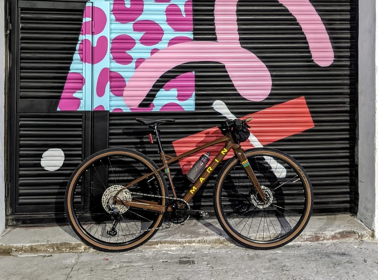 Marin DSX 2 with a bar bag and bottle leaning against a colourful shutter in town, used as a commuter.