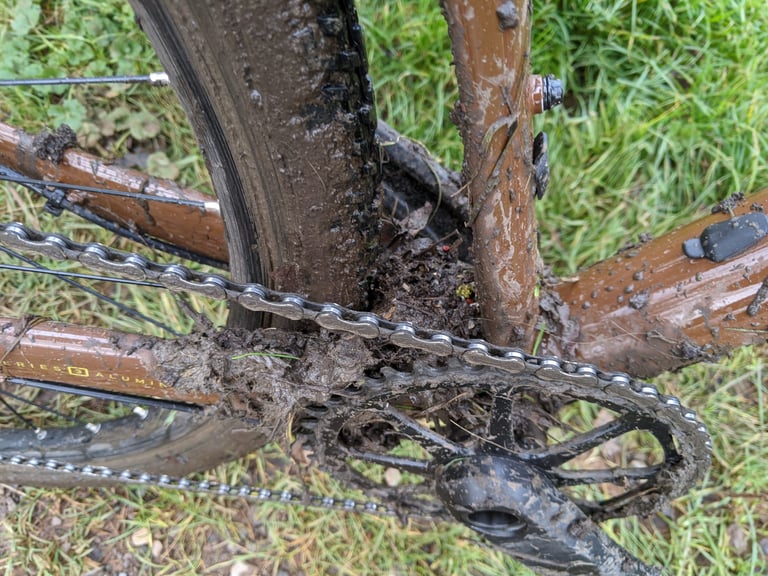Mud and debris packed around the chainring, rear tyre and bottom bracket shelf of the Marin DSX 2 on wet grass.