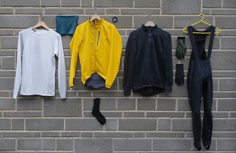 Velocio Alpha System winter kit on a brick wall: base layer, collar, yellow soft shell, Alpha jersey, gloves and bib tights.
