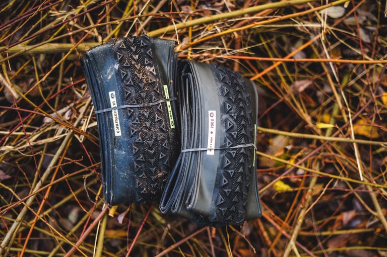 Pair of folded Ultradynamico Rosé tyres tied with straps, lying on twigs and brambles.