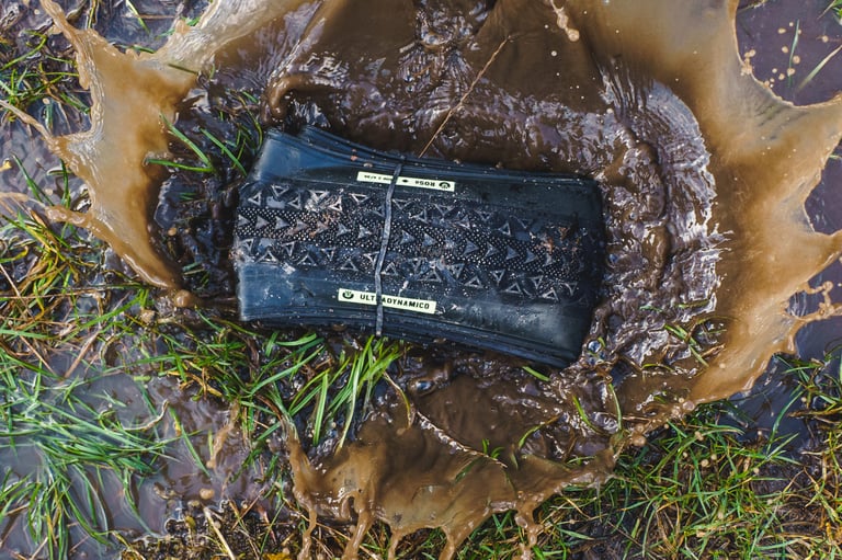 Ultradynamico Rosé Robusto tyre rolled and tied, lying in a muddy puddle with the water splashing up.