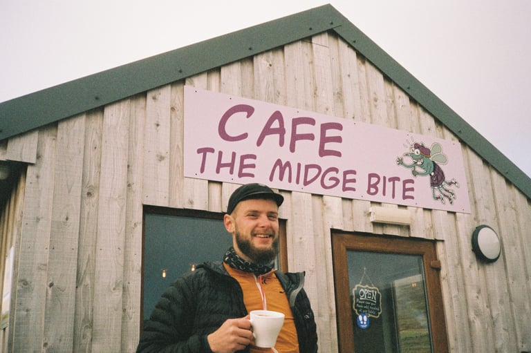 Marcus Nicolson holds a mug outside the Midge Bite Café in Achnasheen on the fixed-gear ride west.