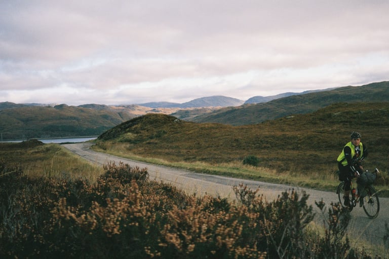 Fixed-gear tourer rides a quiet road through heather-covered hills beside a loch in the north-west Highlands.