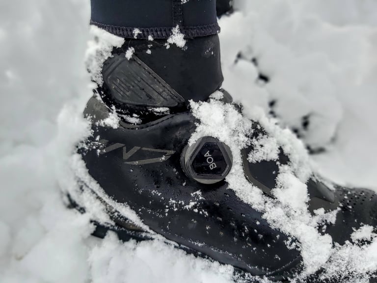 Close-up of a snow-covered Shimano MW7 boot, showing the BOA dial, neoprene cuff and velcro strap.