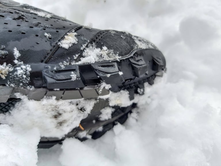 Toe of a Shimano MW7 boot in snow, showing the rugged rubber tread and toe guard.