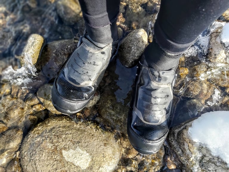 Looking down at Shimano MW7 boots standing on wet stones in a stream, the uppers unmarked after a season of use.