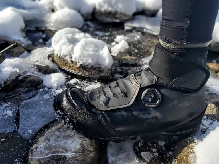 Shimano MW7 boot on an icy rock, showing the BOA L6 dial, the flap covering the laces and the Gore-Tex logo.