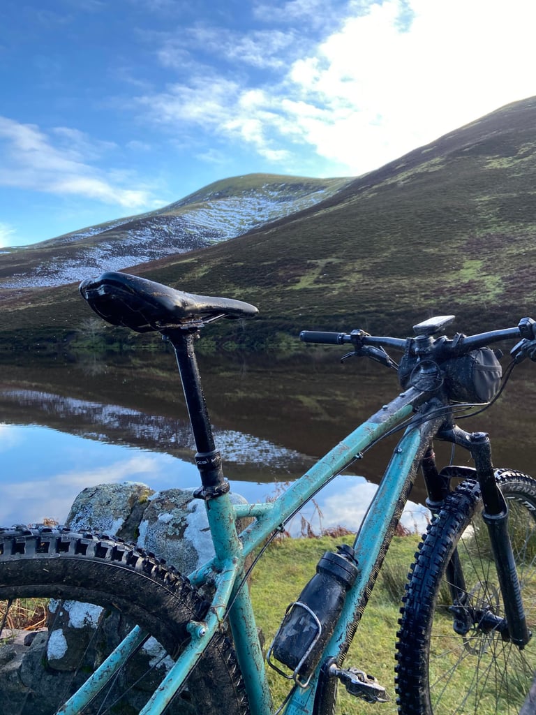 Cale AL saddle, dropper post and bottle cage from behind, with a Pentland reservoir and snowy hillside beyond.
