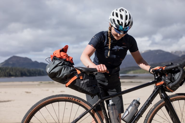 Rider adjusts the Ortlieb seat pack on a gravel bike on a loch-side beach during the 2017 Cairngorms bikepacking trip.