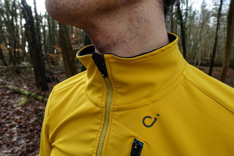 High, soft lined collar and two-way zip of the yellow Velocio Signature soft shell jacket, with the logo on the chest.