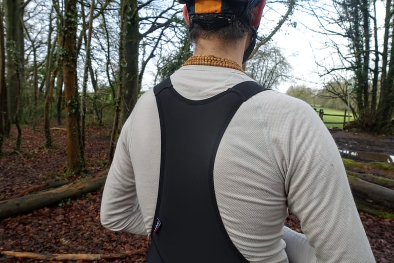 Velocio merino mesh long sleeve base layer in off-white, seen from behind under black bib tight straps.