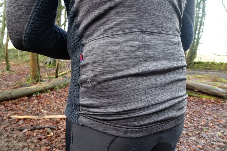 Rear pockets of the grey Velocio Alpha long sleeve jersey, with the Velocio logo and a small colour tag on the side seam.